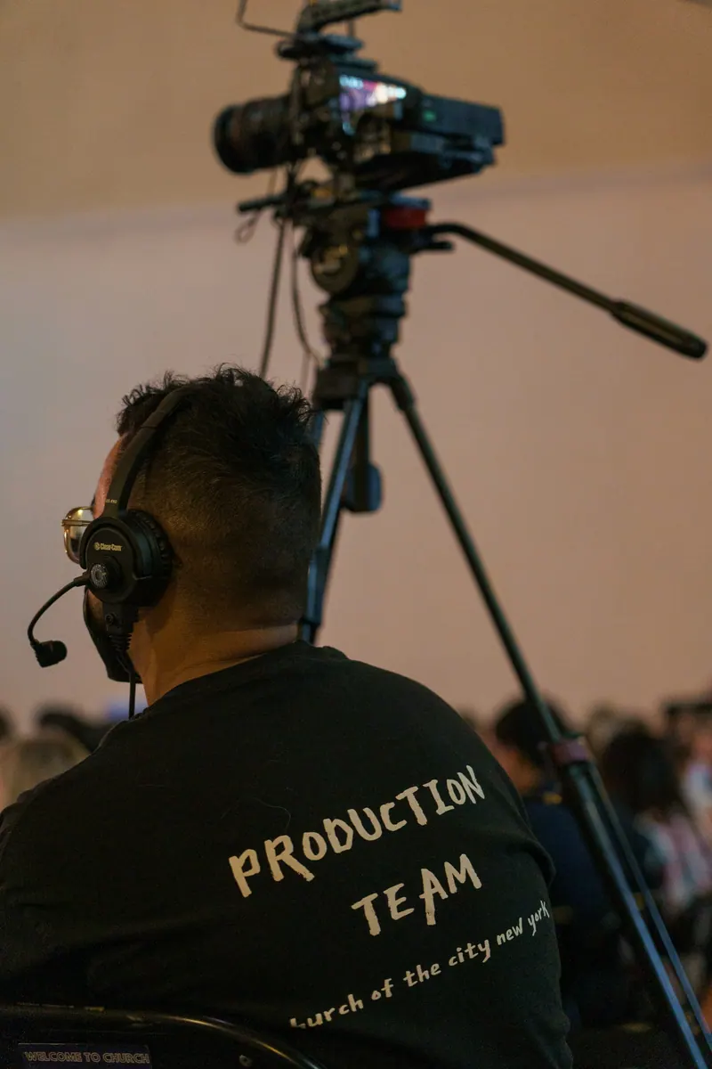 Camera operator with headset behind a broadcast camera at a live event, event videography