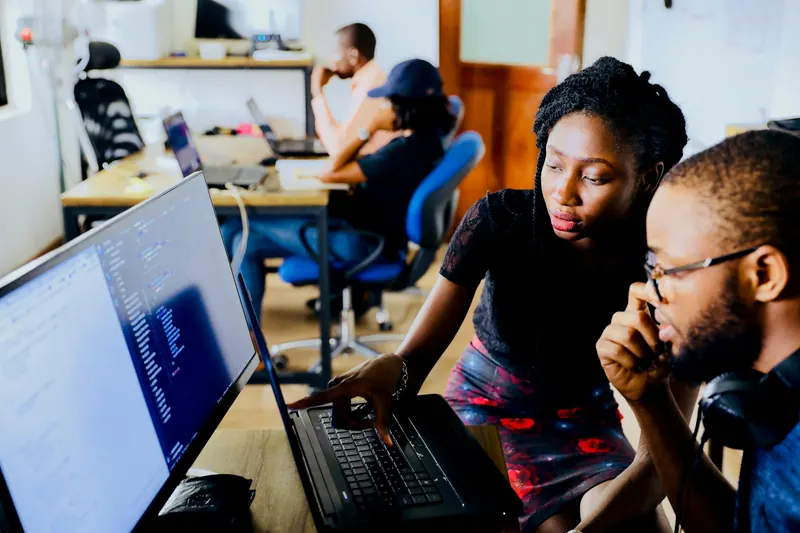 Colleagues reviewing code on a laptop in an open plan office, workplace photography