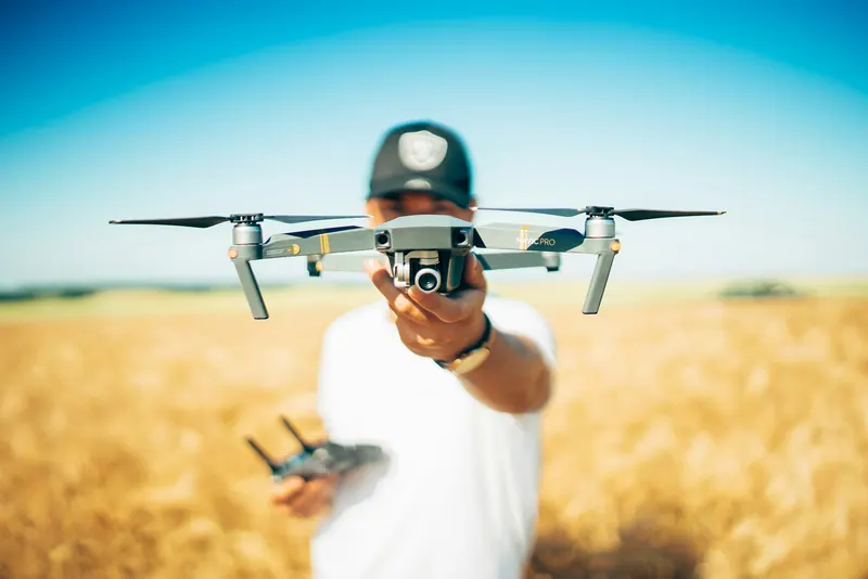 Drone pilot holding a quadcopter towards the camera in a golden wheat field, aerial videography