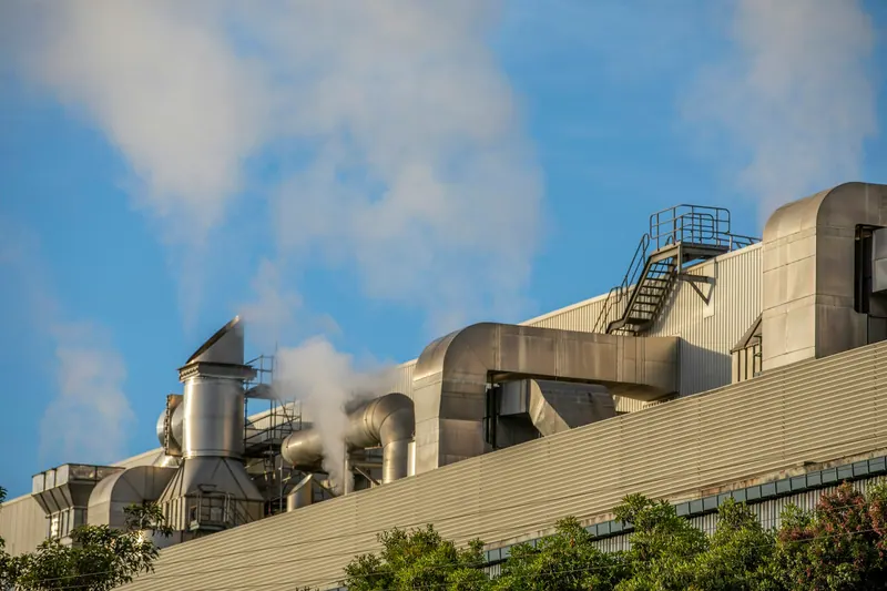 Factory rooftop ductwork and steam under a blue sky, industrial exterior photography
