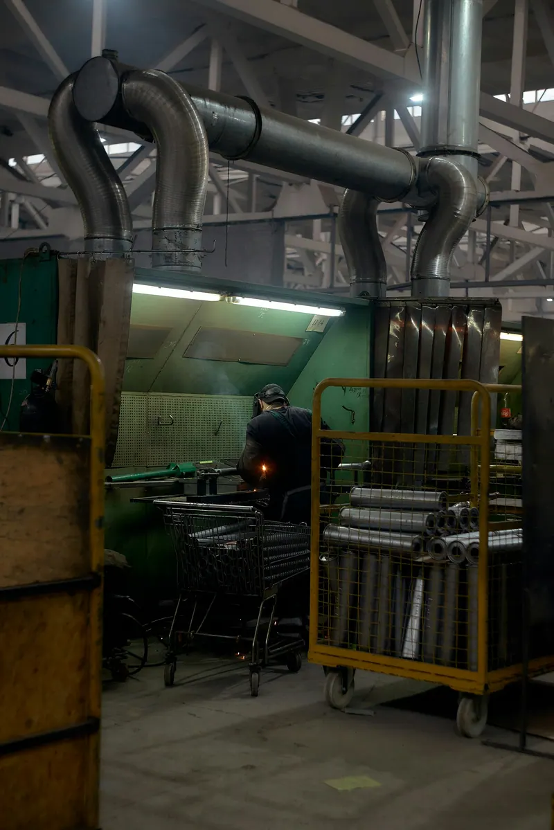 Factory workshop interior with ducting and a worker at a metalworking line, industrial photography