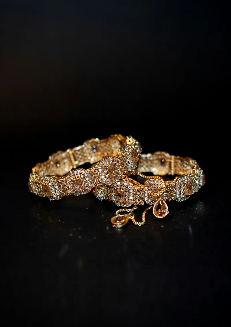 Pair of ornate gold bangles on a black background, low-key jewellery photography
