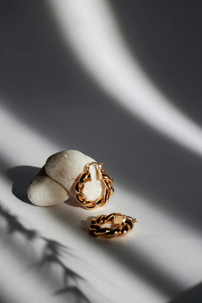 Gold earrings on a stone in hard light with graphic shadows, editorial jewellery photography