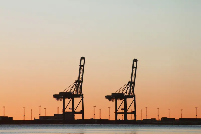 Two port cranes silhouetted against an orange sunset, industrial and logistics photography