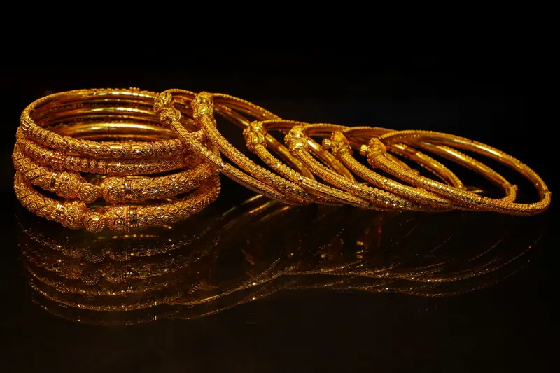 Stack of gold bangles on a reflective black surface, jewellery photography