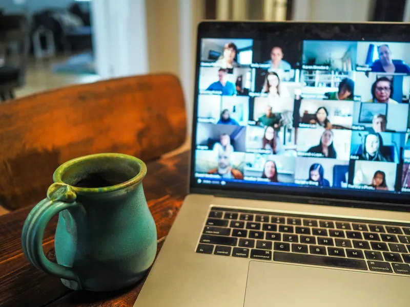 Laptop showing a multi-person video call beside a ceramic mug, remote training session
