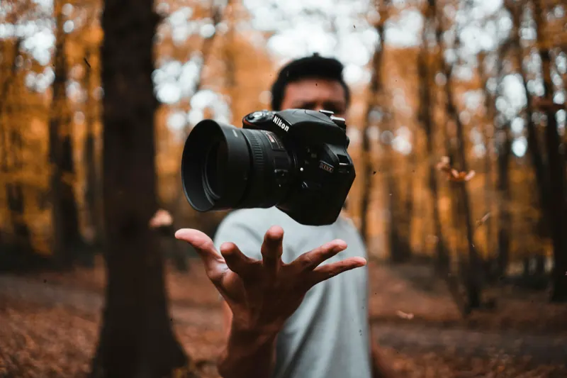 Videographer tossing a DSLR camera in an autumn forest, creative videography
