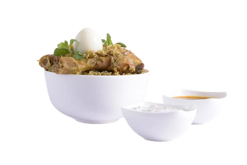 Chicken biryani topped with a boiled egg and fresh mint in a white bowl, served with raita and gravy for restaurant menu photography in Pune