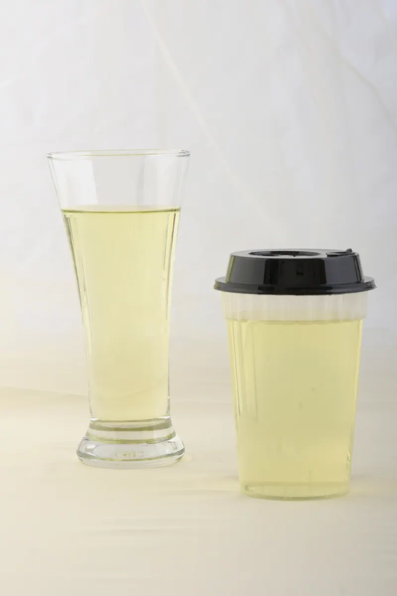 Pale yellow citrus cooler in a pilsner glass next to a takeaway cup with a black lid, clean beverage photography for a cafe brand