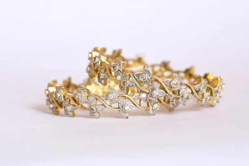 Pair of gold and diamond bangles with floral detailing on a soft white background, macro jewellery photography in Pune