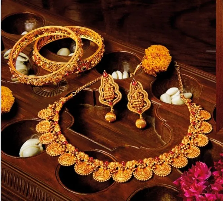 Gold temple jewellery necklace, bangles and jhumkas displayed on a carved wooden tray with marigold flowers, jewellery photography in Pune