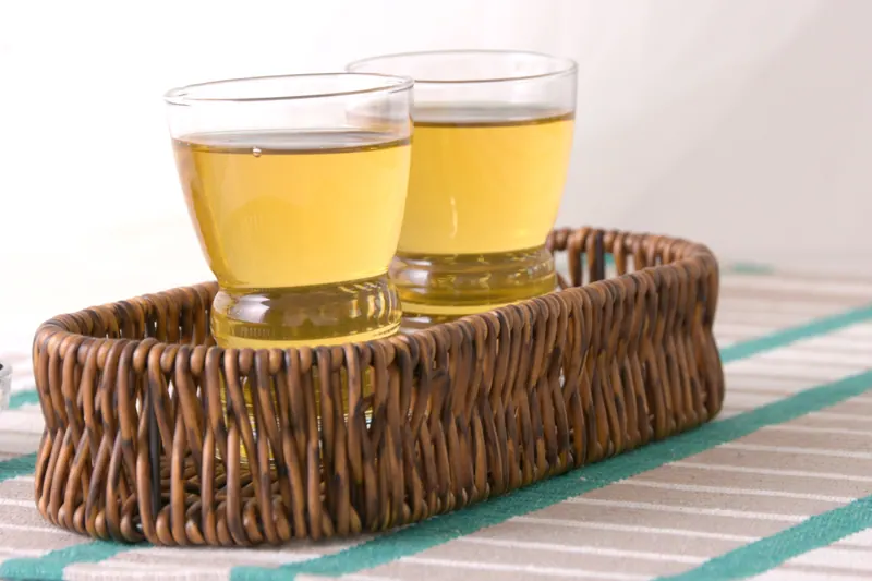 Two glasses of golden tea in a woven wicker tray on a striped cloth, styled beverage photography