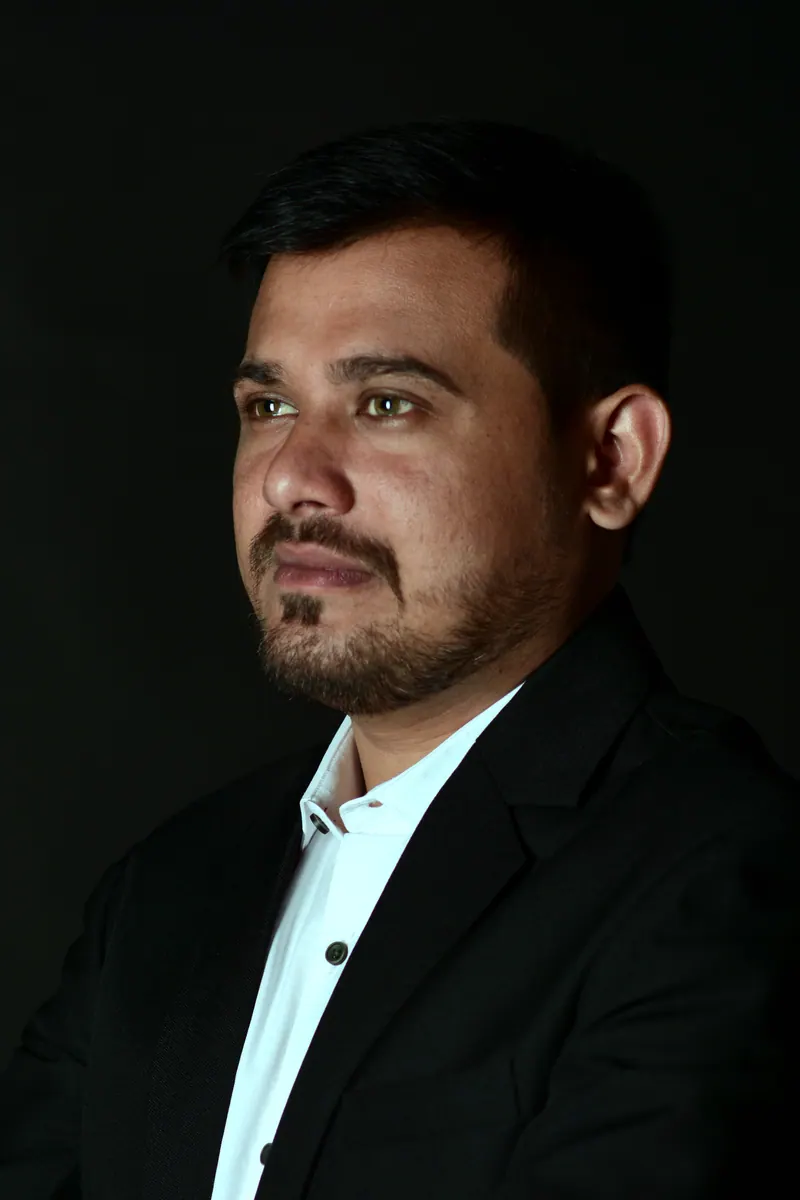 Low-key executive portrait of a man in a black blazer, side-lit against a dark background