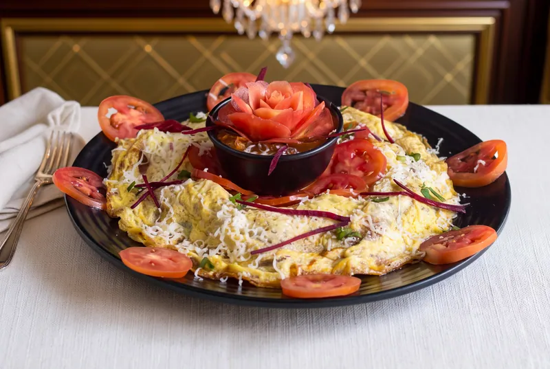 Plated omelette ringed with tomato slices and a tomato rose garnish on a black plate, restaurant food photography in Pune