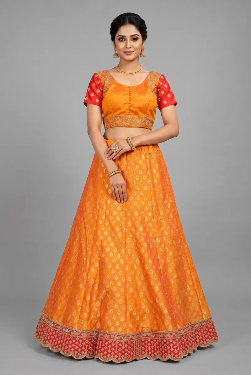 Model in an orange brocade lehenga choli with a red border on a grey studio backdrop, ethnic wear fashion photography in Pune