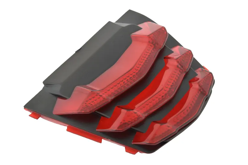 Stack of red moulded automotive lenses with black trim photographed on white