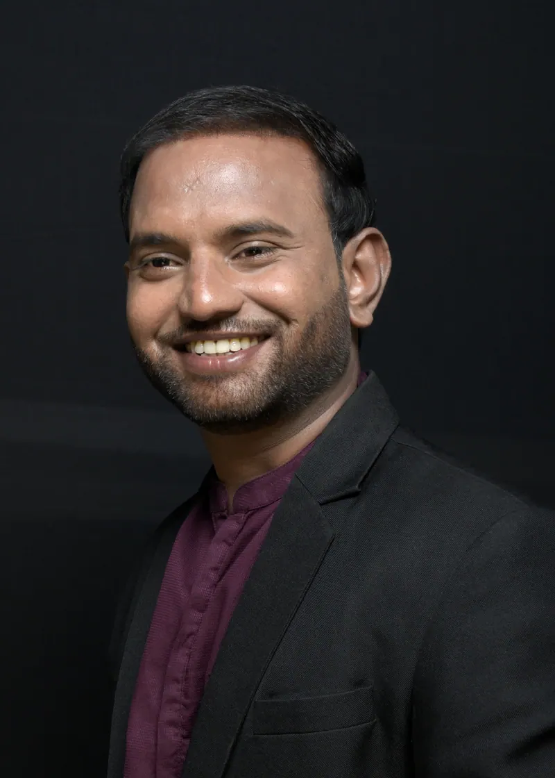 Smiling founder in a black jacket and maroon shirt, personal branding portrait against a dark backdrop