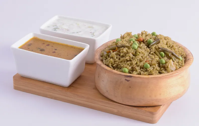 Vegetable pulao in a rustic clay bowl with raita and curry on a wooden serving board, food styling and photography in Pune